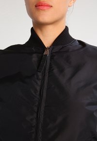 Zwarte bomberjas met ritssluiting en geribbelde kraag. Het materiaal ziet er glad uit met een glanzende textuur.