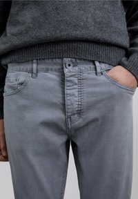 Grå bomuldsbukser med fladt frontstykke, knaplukning og sidelommer. Blød tekstur med subtile syningsdetaljer.