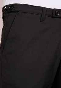 Czarne spodnie materiałowe o gładkiej fakturze, z dwoma czarnymi guzikami w pasie oraz dopasowanym kroju z delikatnymi detalami stębnowania.