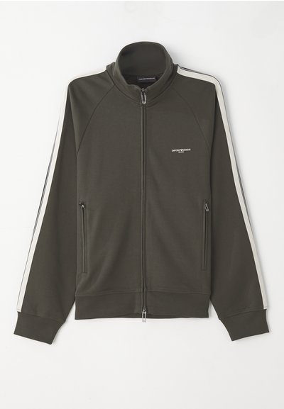 Casaco verde oliva escuro com fecho, com uma superfície texturizada, detalhes em faixa branca nas mangas e dois bolsos laterais com fecho.