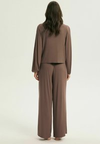 Brązowy komplet wypoczynkowy składający się z luźnej bluzki z długim rękawem i spodni z szerokimi nogawkami, wykonany z miękkiego materiału o gładkiej fakturze.
