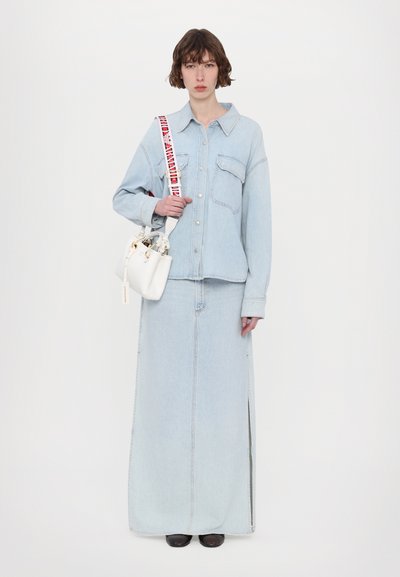 Light blue denim jacket with a collar and front pockets paired with a matching long denim skirt featuring a side slit. White handbag with a colorful strap.