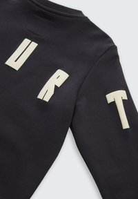 Zwarte sweatshirt met crème blokletters waarop "URT" op de borst en mouw staat. Het materiaal lijkt glad met een ronde hals.