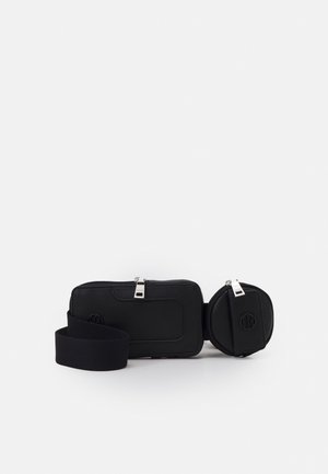 Banane noire avec deux compartiments zippés et une bandoulière réglable, conçue pour porter des affaires personnelles les mains libres.