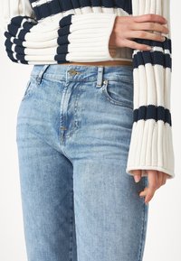 Suéter de punto con rayas blancas y navy, combinado con jeans de mezclilla azul claro, que cuentan con un diseño clásico de cinco bolsillos y un cierre de botones en la parte delantera.
