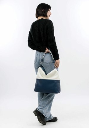 Beige and navy blue shoulder bag with a textured finish, featuring a v-shaped top, braided strap, and silver hardware accents.