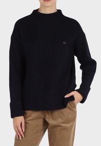 Maglione a coste blu navy con collo alto, vestibilità ampia e maniche lunghe. Dettaglio del logo rosa piccolo ben visibile sul petto.