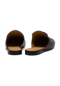Mule in pelle nera con retro aperto, punta rotonda e suola piatta. Presenta solette color cammello e un delicato dettaglio di cucitura.