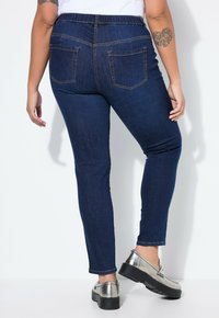 Tmavě modré džínové kalhoty s pružným pasem a dvěma zadními kapsami, doplněné o stříbrné metalické platformové boty.