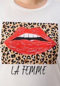 T-shirt blanc avec un graphique de lèvres rouges sur un fond léopard, avec le texte "LA FEMME" en gras sous l'image.