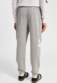 Grijze sweatpants van zacht materiaal met een elastische tailleband. Bevat witte chevronpatronen aan de zijkanten en taps toelopende, aangeknipte enkels.