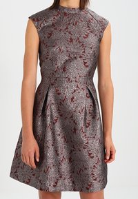 Bezramínkové šaty v burgundské barvě s metalickými květinovými vzory, přiléhavým korzetem a rozšířenou sukní s decentními bočními sklady.