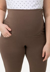Leggings marroni a vita alta con una texture liscia, tasche laterali e cuciture dettagliate. Abbinati a una maglietta bianca con pois neri.