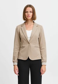 Beiger Blazer mit tailliertem Schnitt, Reverskragen und Knopfverschluss. Verfügt über zwei seitliche Taschen und gestreiftes Material an den Ärmeln.
