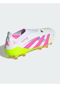 Bottine de football blanche avec des accents rose vif et jaune, présentant un dessus texturé, un design à enfiler et une semelle à crampons distincte pour une traction optimale.