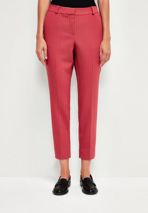Pantalons rouges à rayures avec une coupe ajustée, coupés au niveau de la cheville, présentant un devant plat et des passants de ceinture, associés à des mocassins noirs.