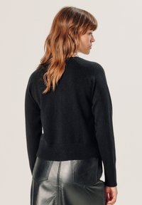 Schwarzer gestrickter Pullover mit geripptem Saum, langen Ärmeln und Rundhalsausschnitt. Kombiniert mit einem schwarzen Leder-Bleistiftrock.