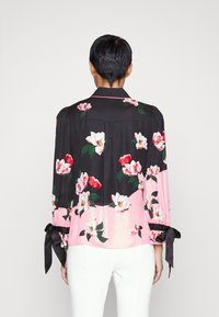 Blusa di seta con motivo floreale, con fiori bianchi e rossi su uno sfondo nero e rosa, maniche lunghe con polsini legati.
