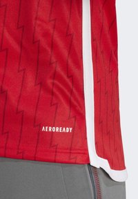 Red athletic shirt featuring lightning bolt pattern, made from breathable fabric with white accents and "AEROREADY" logo near the hem.