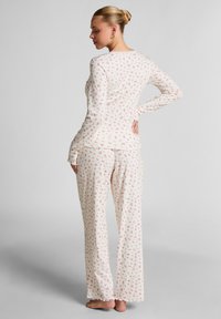 Long-sleeve pajama set in white with a floral print in pink. Soft fabric, relaxed fit, and scalloped edges on cuffs and pants.