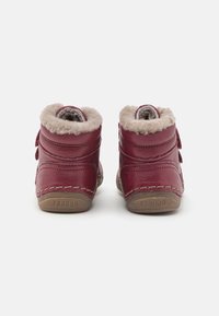 Un paio di stivali per bambini in pelle rossa con fodera in pelliccia sintetica beige, visti da dietro su uno sfondo bianco.