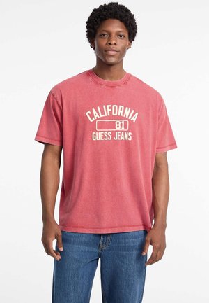 Rode katoenen t-shirt met korte mouwen, voorzien van de tekst "CALIFORNIA 81 GUESS JEANS" in het wit. Gepaarde met blauwe denim jeans.