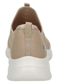 Zapatilla deportiva sin cordones en color beige, con parte superior de tela texturizada, cuello acolchado y suela de goma blanca. Presenta un tirador y un acento de logotipo.