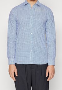 Camisa azul de manga larga con un estampado de formas circulares y cuadradas, con un collar entallado y cierre de botones en la parte delantera.