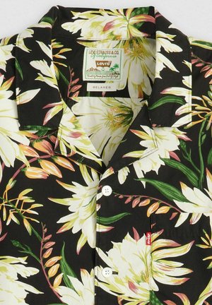 Camisa de manga corta negra con un patrón floral en blanco y tonos pasteles. Presenta un cuello relajado, dos botones blancos y una pequeña etiqueta de la marca.