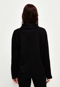 Pullover oversize nero con colletto alto, realizzato in tessuto morbido; presenta spalle cadute e una vestibilità rilassata; design minimalista.
