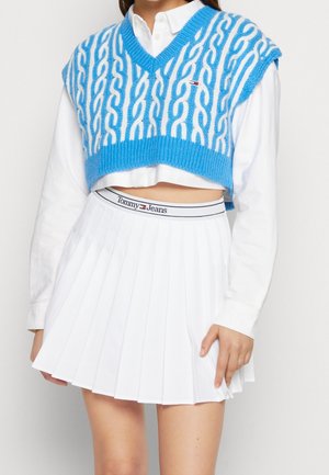 Blå strikket vest med hvid kabeldesign, båret over en hvid skjortekrave. Har en plisset hvid nederdel med en mærkevare-bælte.