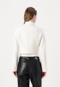 Blazer blanc coupé avec un tissu texturé, col à revers et manches longues, associé à un pantalon en cuir noir taille haute avec un écusson logo.
