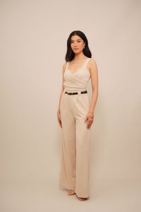 Combinaison beige avec un corsage ajusté, des jambes larges et une ceinture noire. Présente un design croisé à l'avant et des bretelles ajustables. Texture lisse.