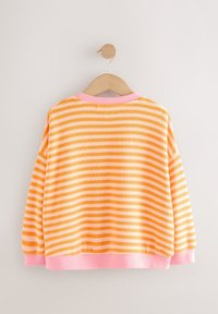 Pull rayé orange et blanc à manches longues avec col, poignets et ourlet roses, suspendu sur un cintre en bois contre un mur blanc.