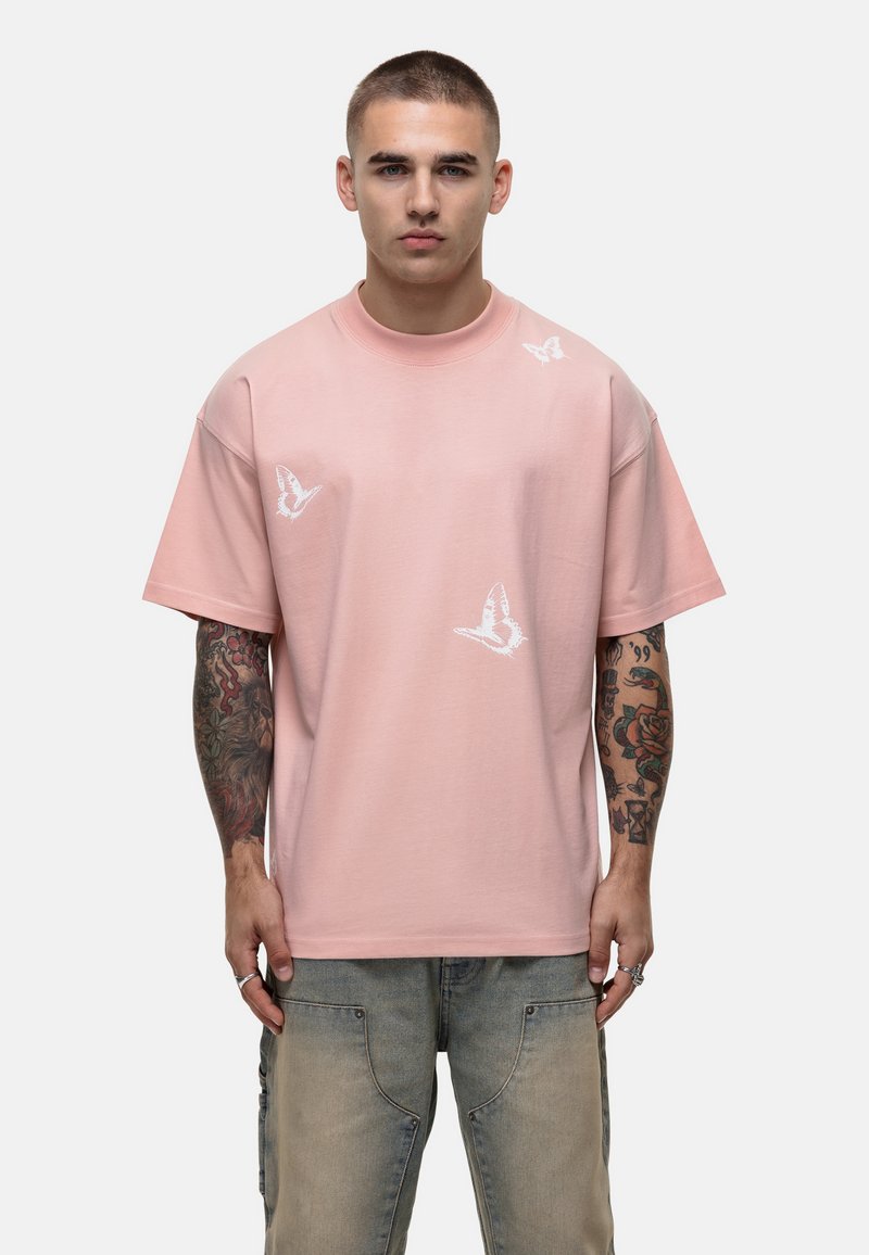 T-shirt en coton rose clair avec un col rond, manches courtes et imprimés de papillons blancs. Présente une coupe décontractée et une texture lisse.