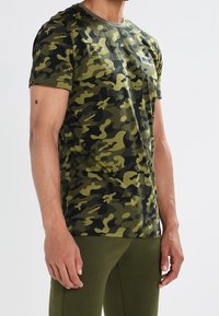 Grön kamouflagemönstrad t-shirt i strukturerad tyg med rund halsringning och korta ärmar. Har en liten logotypapplikation på bröstet.