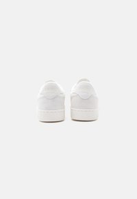 Ζευγάρι λευκά δερμάτινα αθλητικά παπούτσια Reebok, εμφανιζόμενα από πίσω σε απλό ανοιχτό γκρι φόντο.