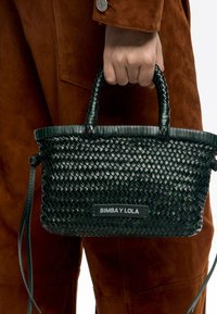 Tkanozelna zelena torba z dvojnimi ročaji, pravokotne oblike, teksturirano površino in črnim logotipom z oznako "BIMBA Y LOLA."