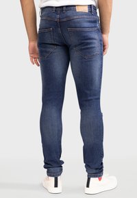 Jeans skinny azul oscuro con una textura de denim suave, que cuentan con una cinturilla de altura media, dos bolsillos traseros y un detalle de costura minimalista.