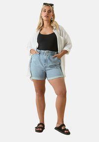 Farkkutrikoot, joissa on käännetty helma, vaaleansininen väri, joustava vyötärö, yhdistettynä mustaan topiin ja yli suuren valkoiseen paitaan. Mustat sandaalit.