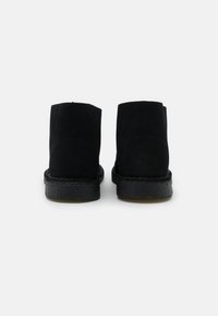 Schwarze Wildleder-Stiefeletten mit abgerundeter Zehenpartie und dickem schwarzem Gummisohle. Mit kontrastierenden Nähten entlang der Sohle und glatter Textur.