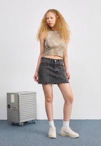 Black denim mini skirt with frayed hem, paired with a beige velvet crop top, worn with white socks and light-colored sneakers.