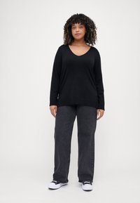 Black long-sleeve v-neck shirt paired with dark gray wide-leg jeans and black-and-white sneakers, presented on a neutral background.