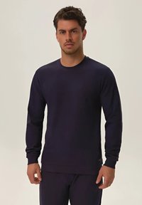 Ciemnofioletowy długi rękaw sweter z okrągłym dekoltem, ściągaczami na mankietach i dolnym brzegu. Miękka tkanina, dopasowany krój, minimalne logo z boku.