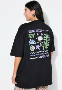 Camiseta negra de gran tamaño con diseños gráficos coloridos en la parte posterior, que incluyen plantas, formas y texto. Material de algodón con un corte relajado.