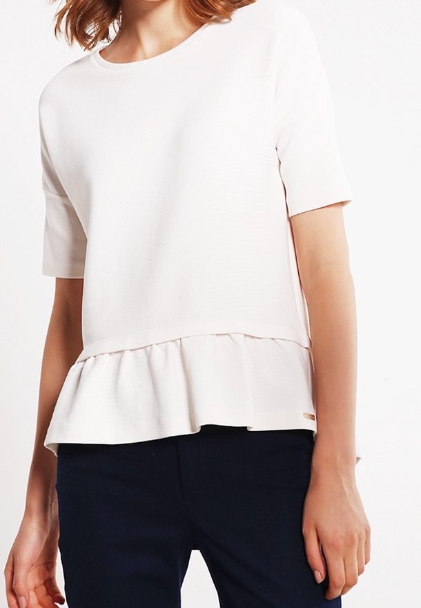 Vit kortärmad topp med texturerad yta, med peplumslut och rund halsringning. Matcher med mörka byxor för kontrast.