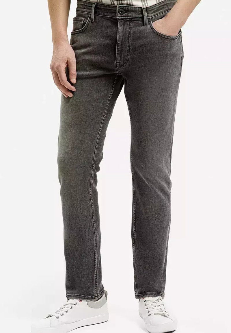 Szare dżinsy o prostym kroju, z pięcioma kieszeniami i subtelnymi detalami przyszycia. Noszone z białymi sneakersami.