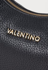 Black textured leather handbag with gold "VALENTINO" logo and zipper detail. Close-up captures the material's grain and shine.