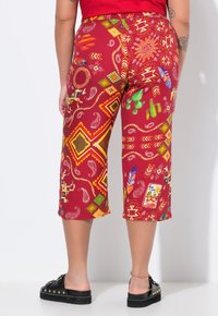 Pantaloni alla caviglia rossi con pattern geometrico e ispirato alla natura in giallo, verde e blu. Vita elasticizzata, vestibilità comoda.