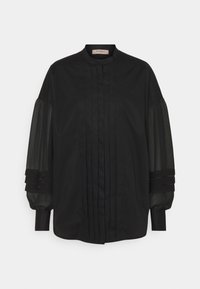 Chemise noire avec col montant, devant plissé et manches bouffantes transparentes avec accents de tissu superposés. Texture lisse et design classique.